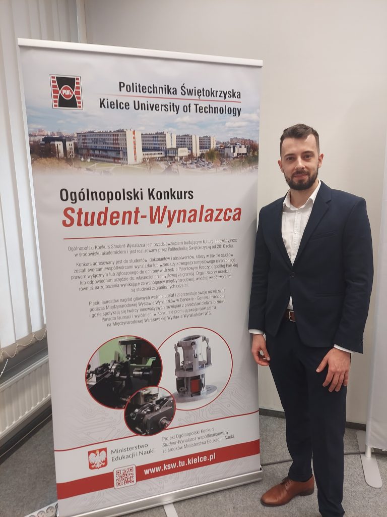 Marcin Jakubiec przy plakacie Konkursu Student-Wynalazca